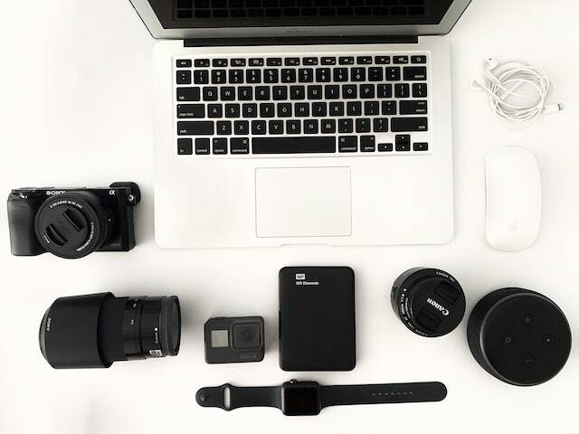 an open laptop and a bunch of camera equipment and lenses on a desk